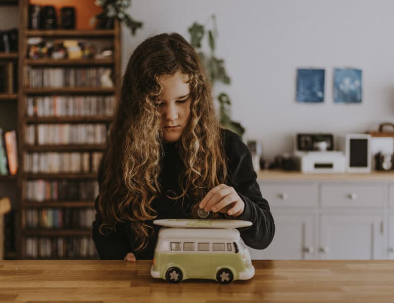 Ein Mädchen wirft Geld in eine Spardose, die aussieht wie in Camper.