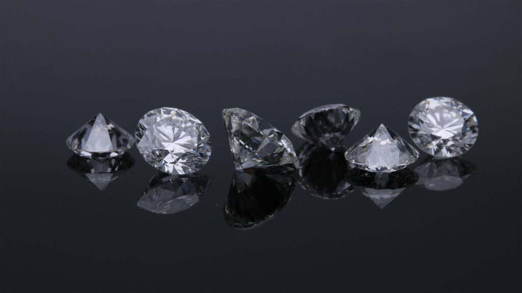 6 Diamanten liegen nebeneinander auf einer schwarzen, glatten Oberfläche.